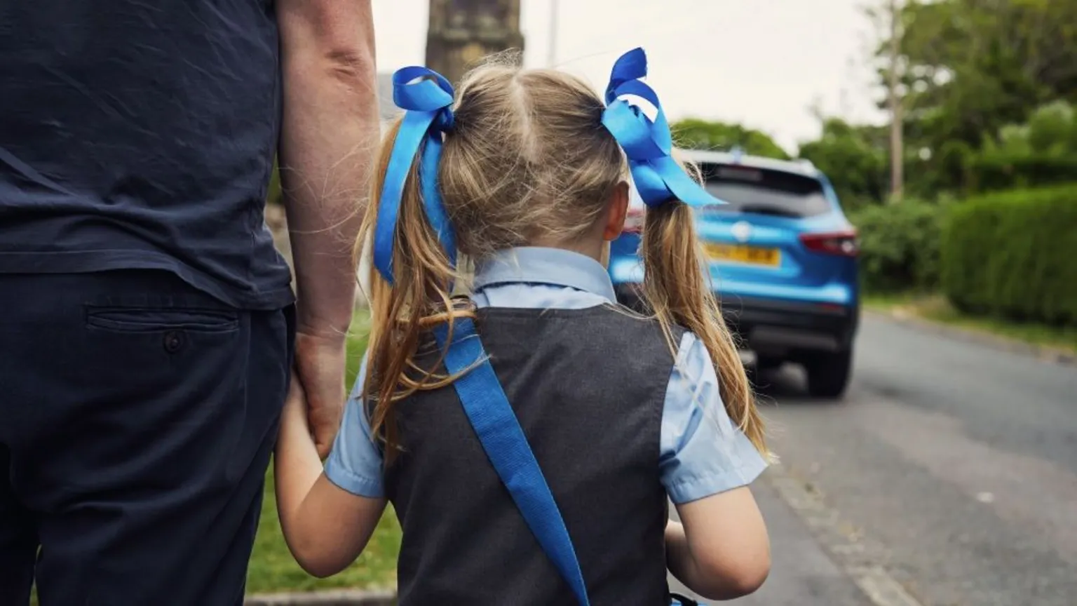 picture of a young girl from behind holding someone's hand, walking down a street
